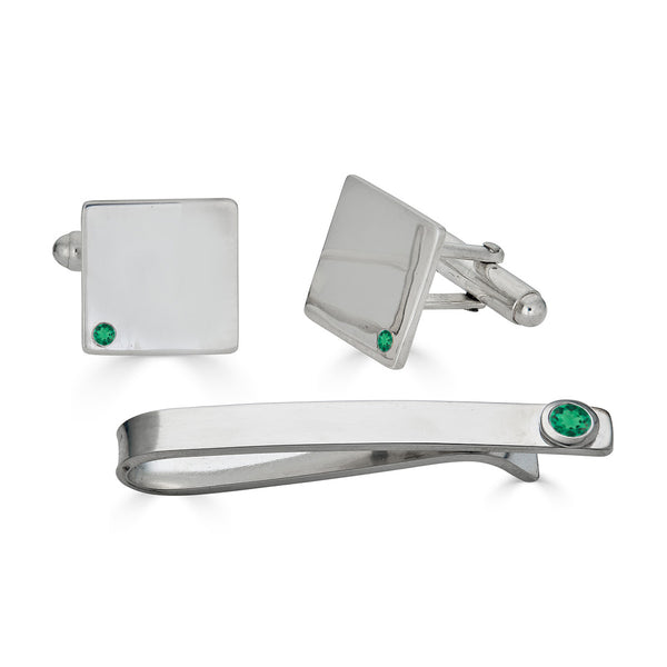 Silver cufflinks and tie clip set with emeralds on a white background