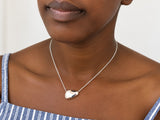 Sterling silver pebble necklace in a shiny finish worn on a model, a smooth rounded pendant resting at the collarbone on a fine adjustable chain.